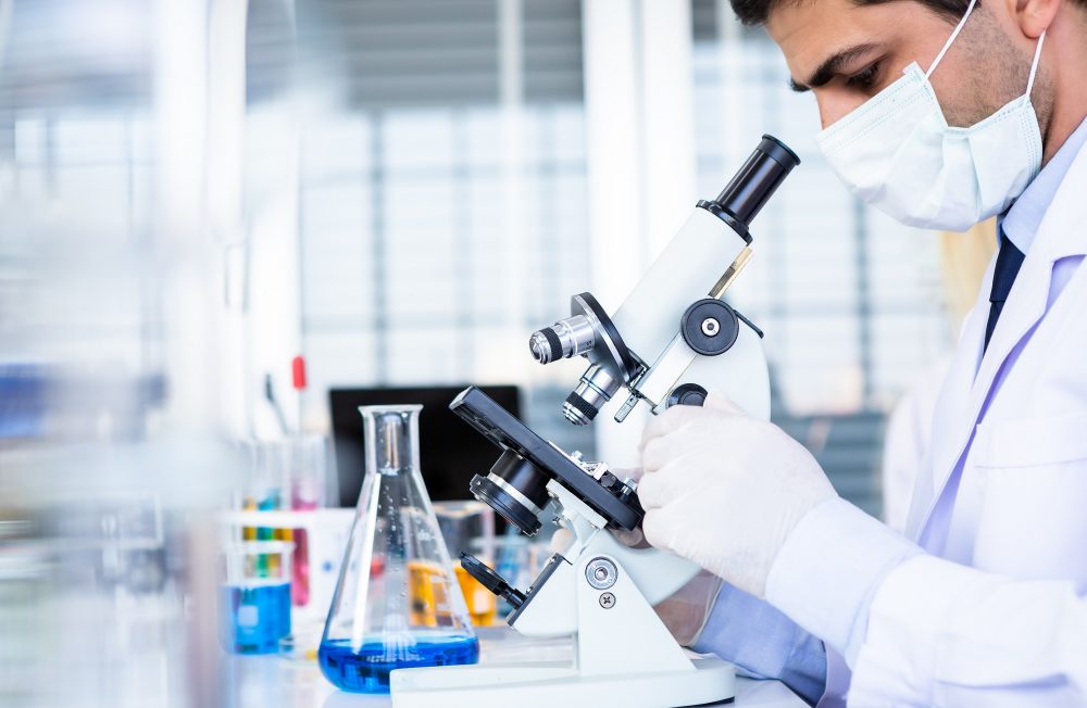 Male scientist working looking at Microscope with sample test tu